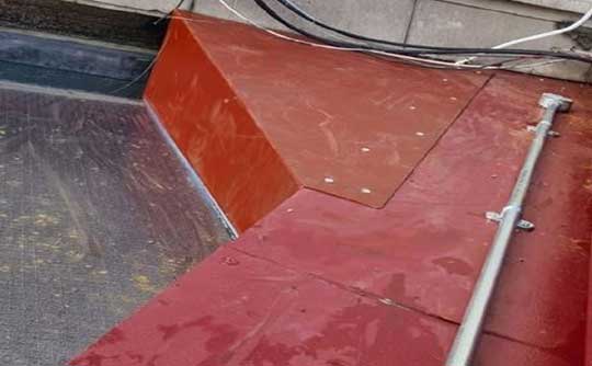 Sheet metal flashing to protect services run on flat roof at London Underground station